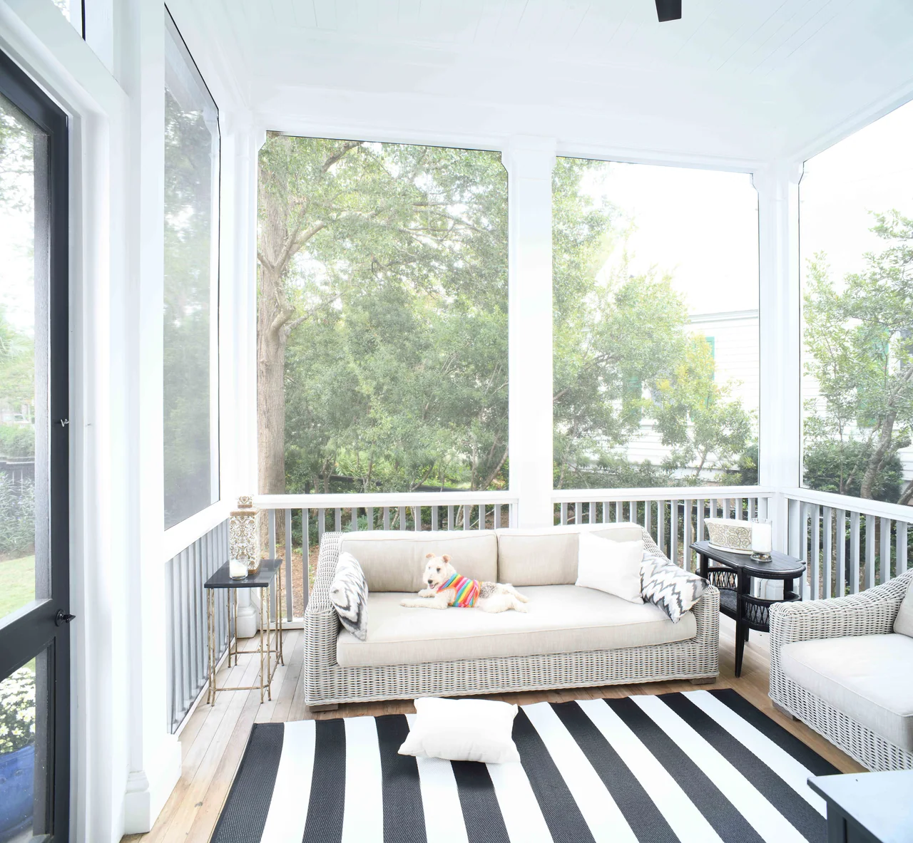 Screened porch with a hanging daybed and striped rug